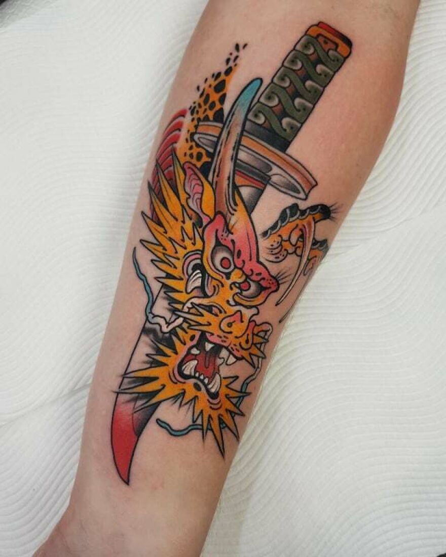 Vibrant dragon tattoo design with sword on forearm, showcasing bold colors and dynamic details.