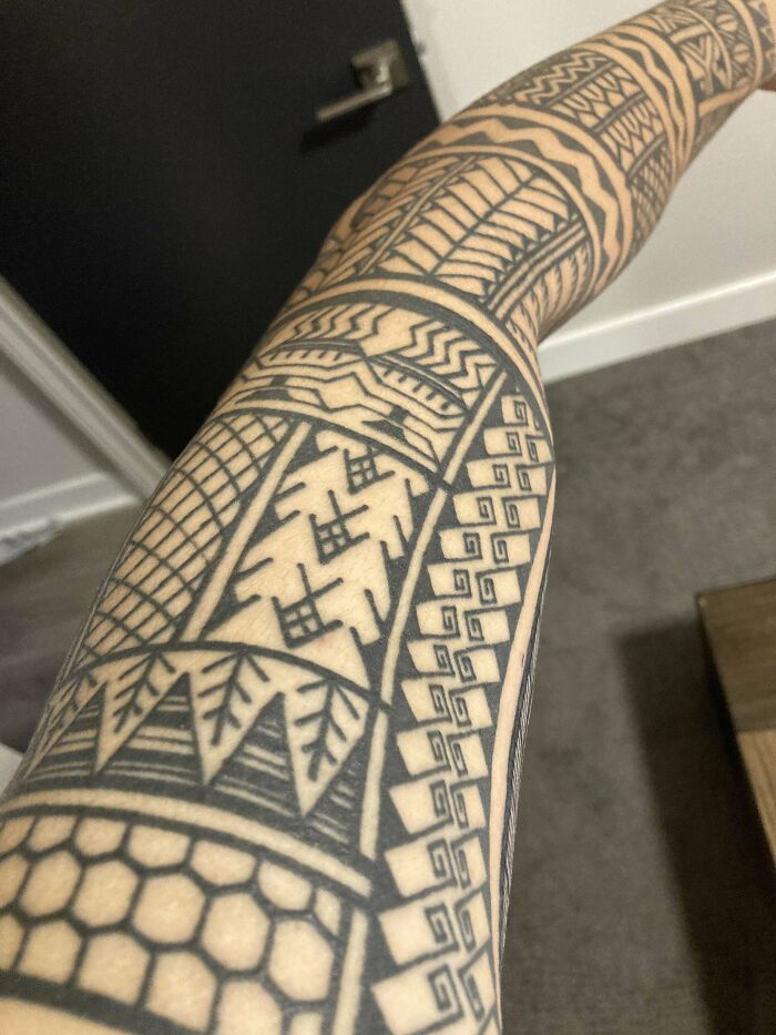 Arm with intricate tribal tattoo design featuring geometric patterns.