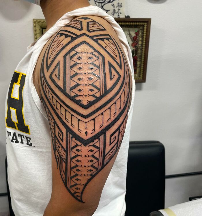 A detailed tribal tattoo design on an upper arm, featuring intricate geometric patterns.