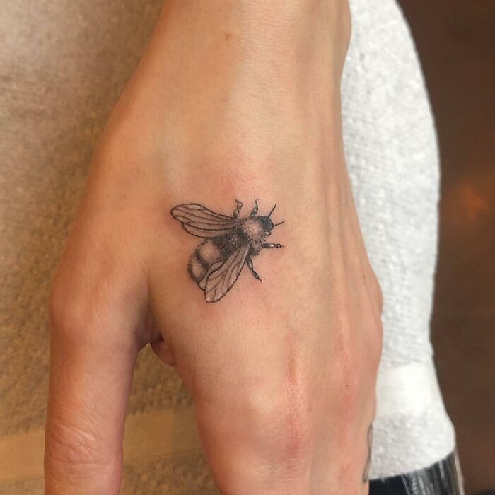 Small hand tattoo of a detailed bee design on the back of the hand.