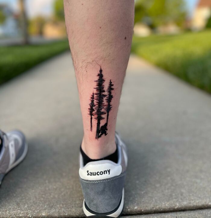 Tattoo of tall trees and a bear on a person's leg, showcasing majestic nature art.