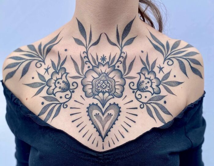 Floral and heart design collarbone tattoo on a person wearing a black top.