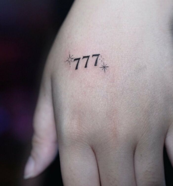 Small hand tattoo featuring the number 777 with star accents.