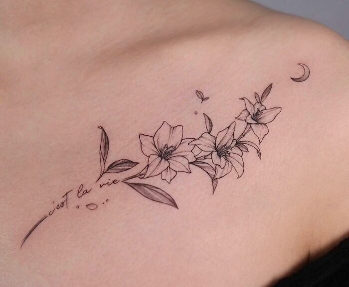 Floral collarbone tattoo with lilies and script, featuring delicate linework for men and women.