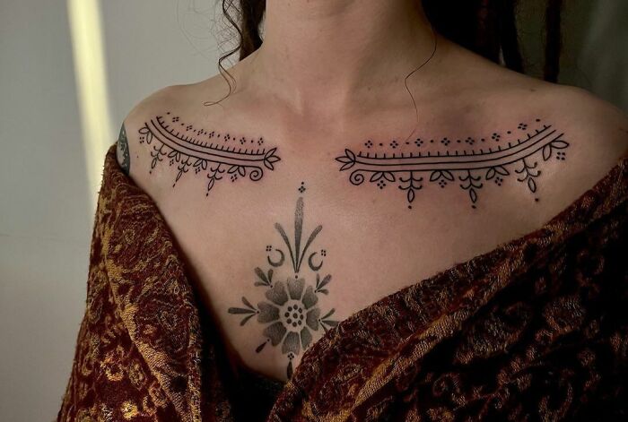 Intricate collarbone tattoos featuring elegant floral designs on a woman's upper chest, wrapped in a patterned shawl.