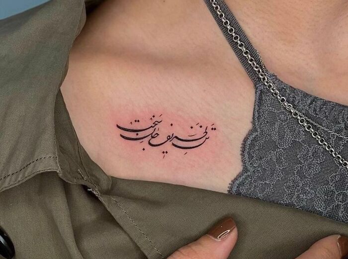 Collarbone tattoo with elegant script, partially covered by a lace top and chain necklace.