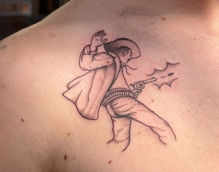 Collarbone tattoo of a cowboy firing a gun, designed with detailed shading.