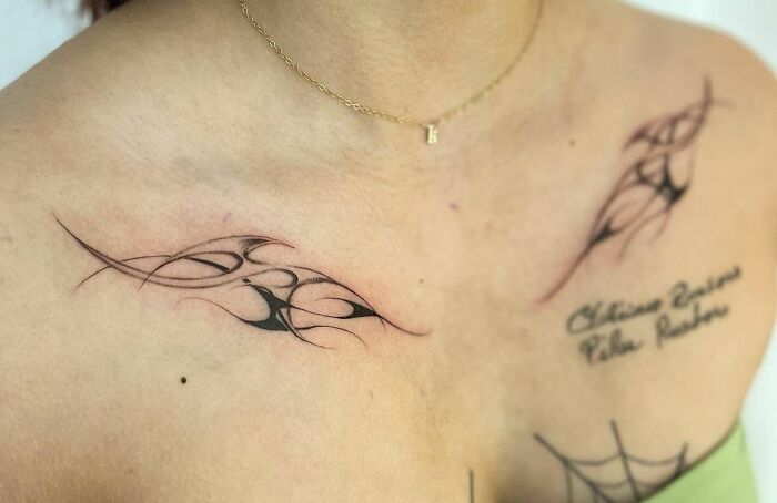 Collarbone tattoos with intricate black tribal designs on a person's skin.