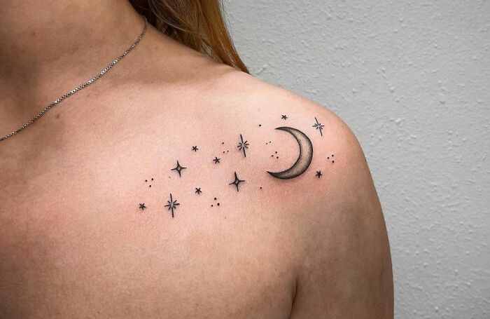 Minimalist moon and stars collarbone tattoo on a woman's shoulder.