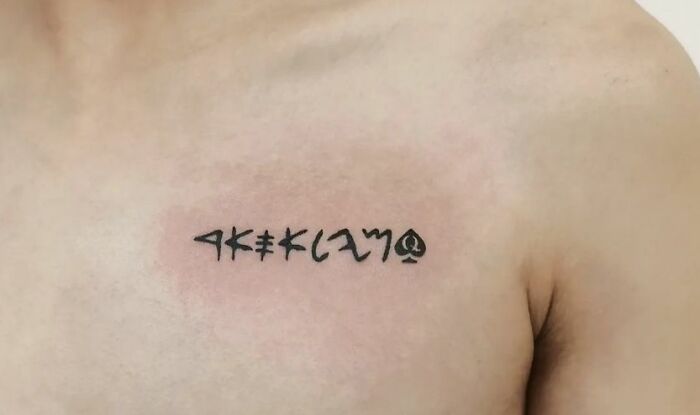 Collarbone tattoo with unique black script design on a person's chest.