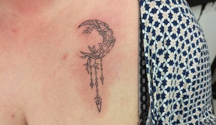 Ornate moon and floral collarbone tattoo design on a person wearing a patterned top.