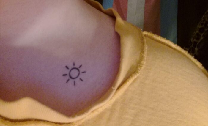 Minimalist sun collarbone tattoo on a person wearing a yellow top.