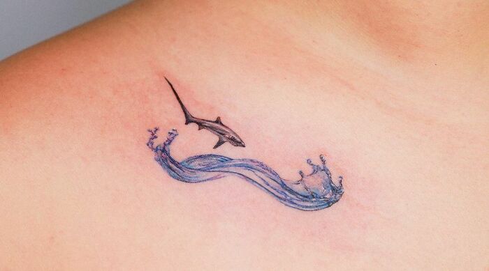 Subtle shark and wave collarbone tattoo on skin, showcasing unique art for men and women.