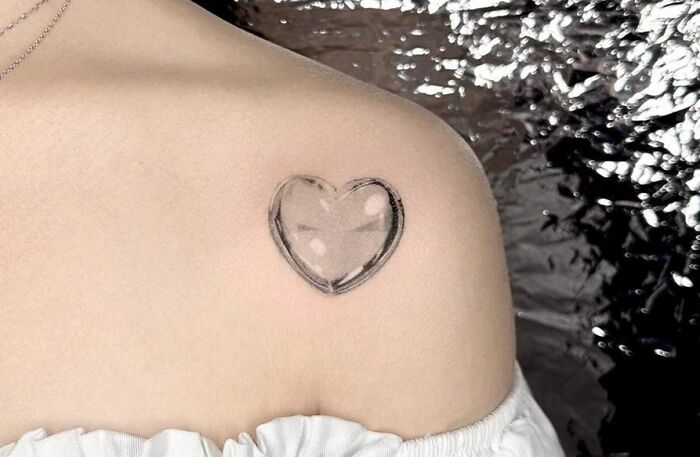 Heart-shaped collarbone tattoo on a person's shoulder in a minimalistic style.