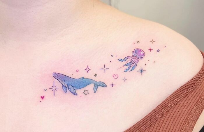 Collarbone tattoo featuring a colorful whale, jellyfish, and stars design.