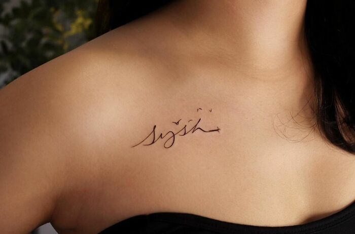 Minimalistic collarbone tattoo on woman with birds and cursive script.
