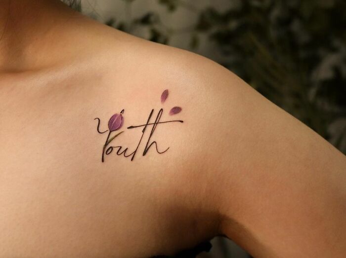 Collarbone tattoo with "Youth" in elegant script and purple flower accents.