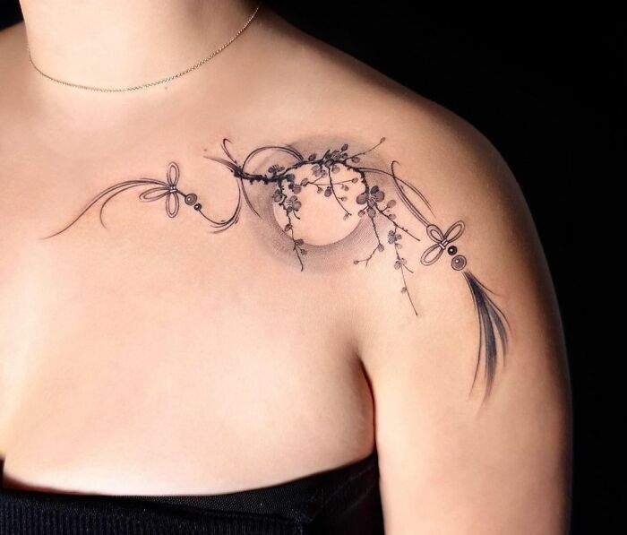 Delicate floral collarbone tattoo on a woman's shoulder, featuring intricate line work and shading.