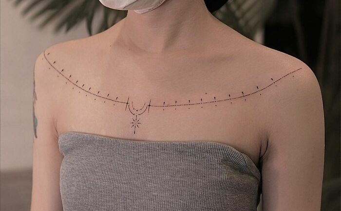 Minimalist collarbone tattoo with geometric design on a person wearing a gray top.