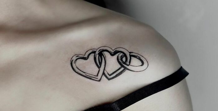 Collarbone tattoo of interlinked hearts and rings on a person's shoulder.