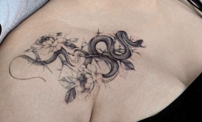 Collarbone tattoo featuring a detailed snake and floral design on a person's skin.