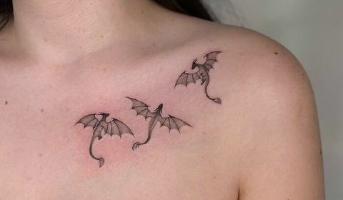 Three small dragon tattoos on a person's collarbone.