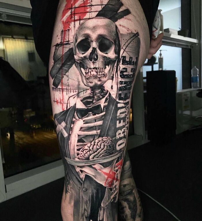 Trash Polka tattoo featuring a skeleton in a suit, holding a brain with bold red and black ink contrasts.