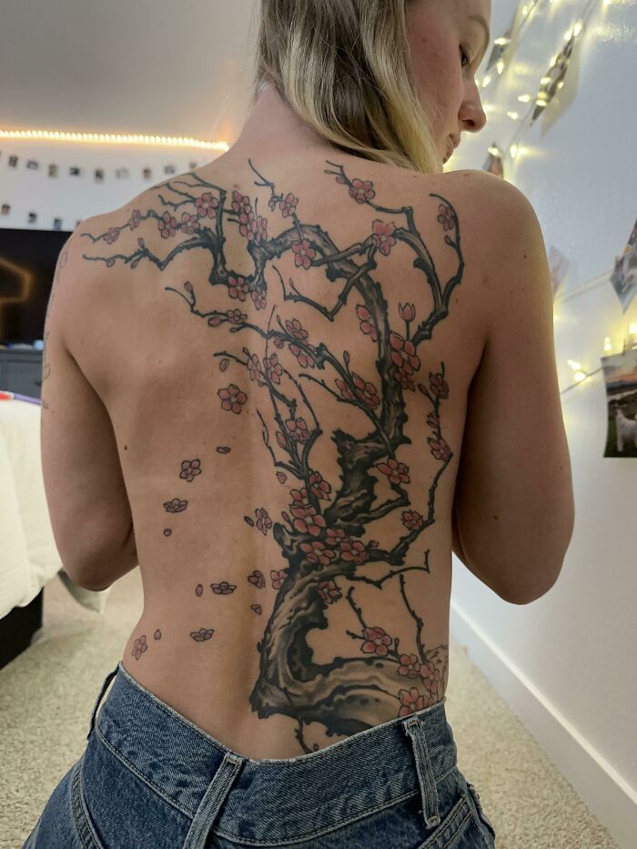 Back tattoo featuring a majestic tree with pink blossoms, showcasing the wonders of nature.