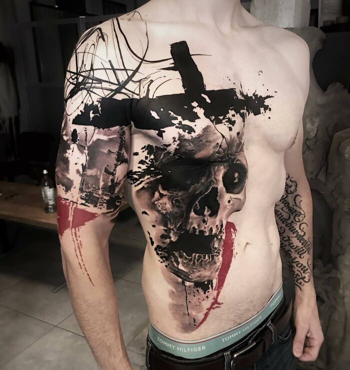 Man with striking Trash Polka tattoo featuring a skull and abstract patterns on chest and arm.