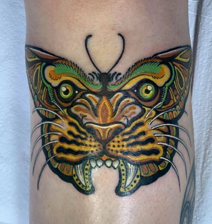 Colorful butterfly tattoo resembling a tiger face, featuring vibrant green and orange patterns.