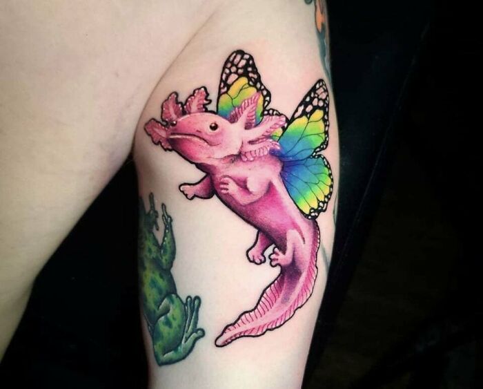 Colorful butterfly tattoo featuring a pink creature with rainbow wings on a person's arm.
