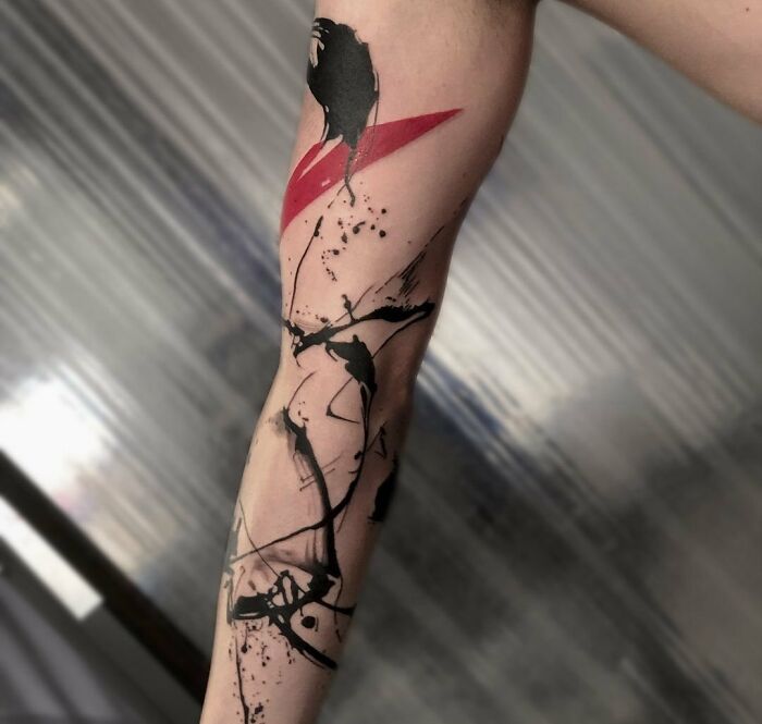 Trash Polka tattoo on arm with red and black abstract design, combining bold strokes and splatters.