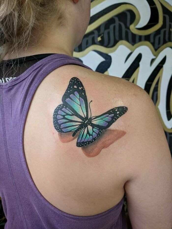 Colorful butterfly tattoo on a woman's shoulder, showing vibrant shades and intricate design.