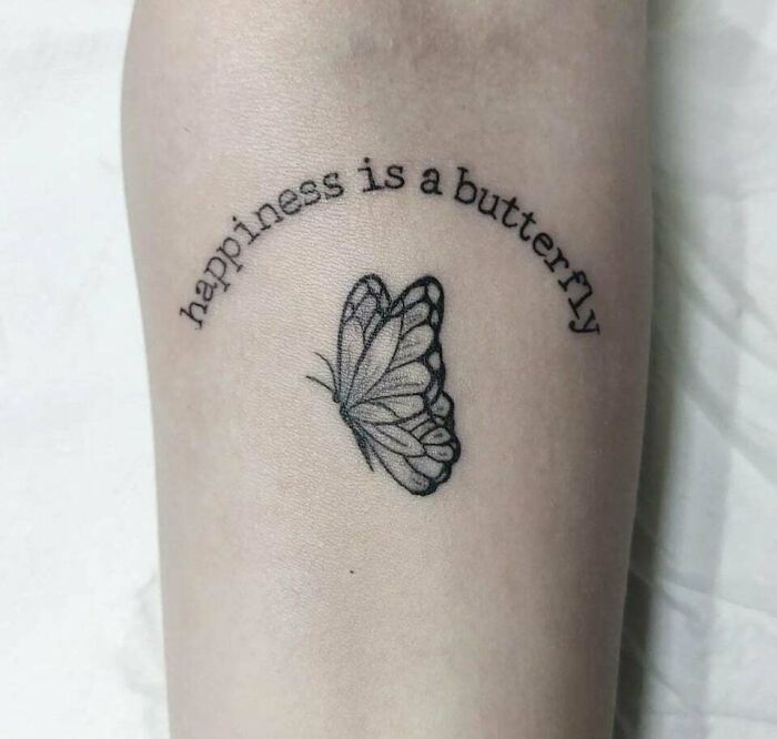 Tattoo of a butterfly with the phrase "happiness is a butterfly" inked above it.