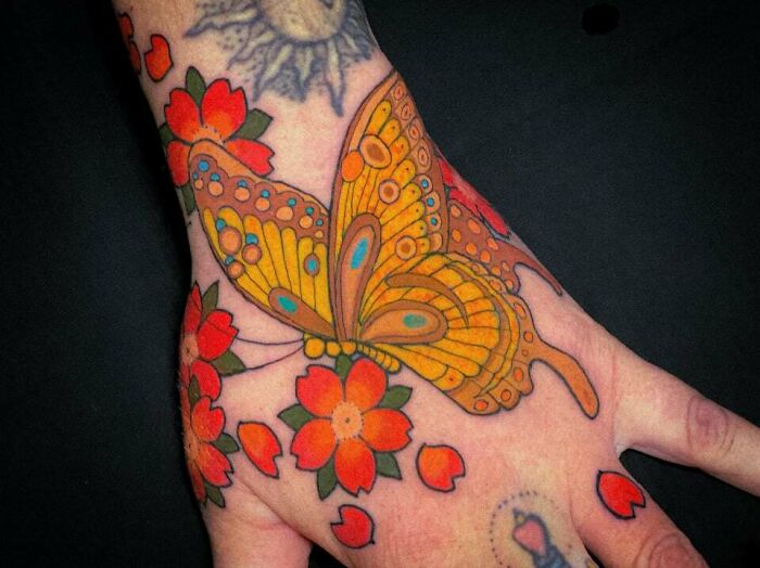 Colorful butterfly tattoo with flowers on a hand, showcasing vibrant and fun design elements.