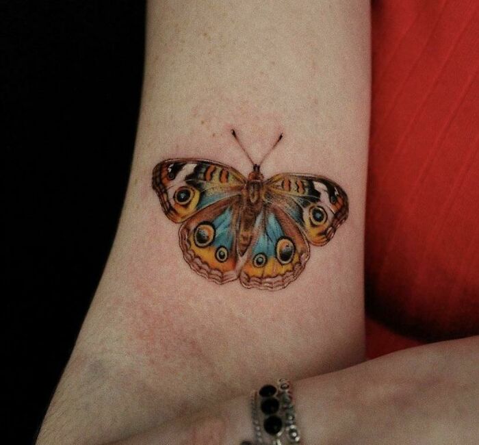 Colorful butterfly tattoo on an arm, showcasing intricate and vibrant design.