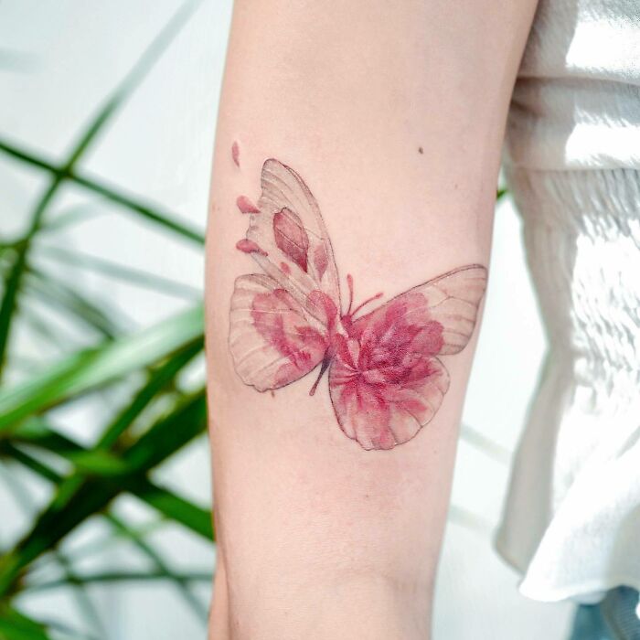 Colorful butterfly tattoo on an arm, showcasing intricate red and pink details.