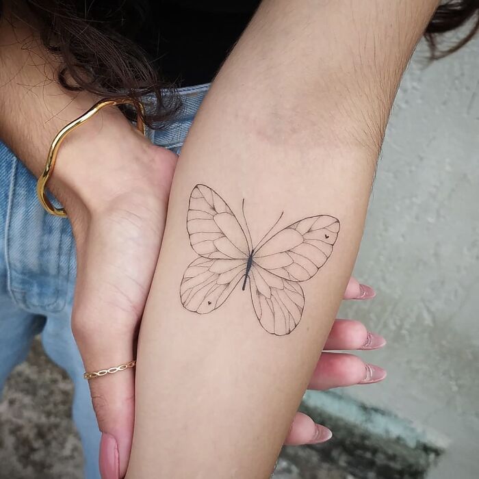 Minimalist butterfly tattoo design on a person's forearm, featuring delicate linework.