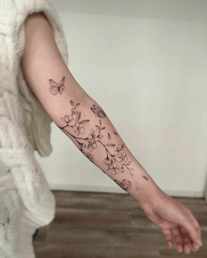 Forearm adorned with a delicate butterfly tattoo and floral design in black ink.