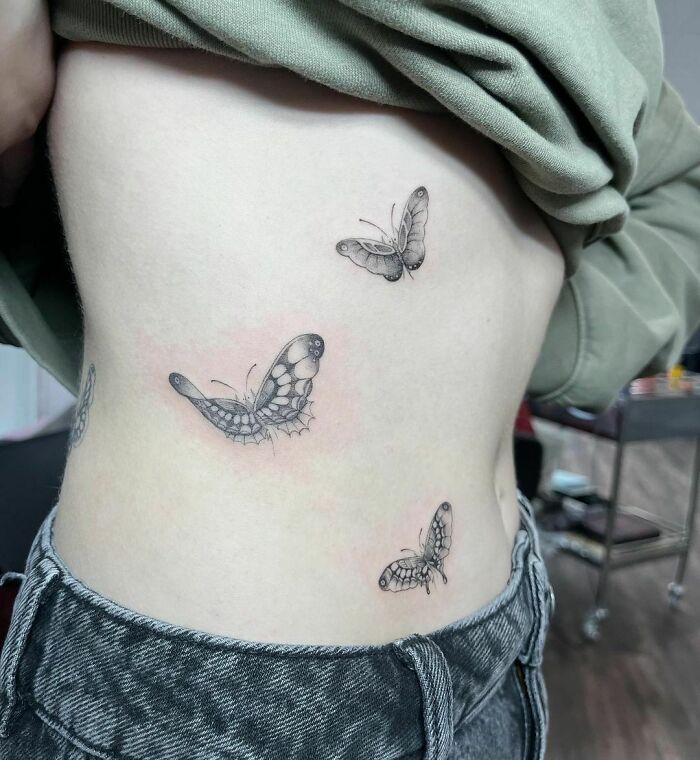 Butterfly tattoos on a person's side, featuring three detailed black ink designs.