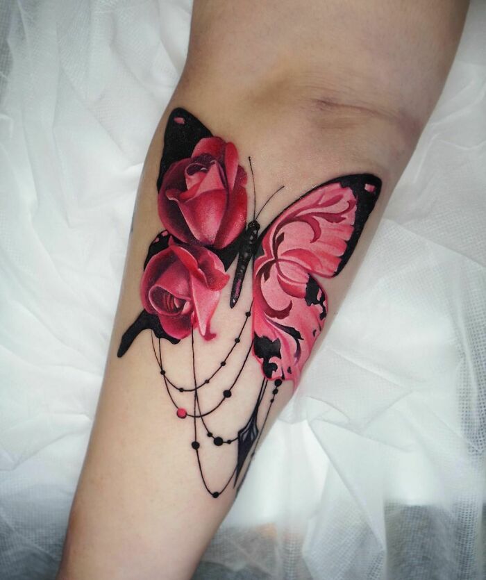 Colorful butterfly tattoo with pink roses and detailed design on forearm.