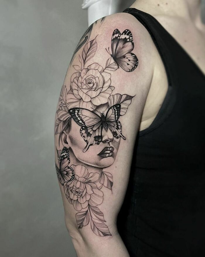 Black and gray butterfly tattoo with roses on arm, featuring face with butterflies.