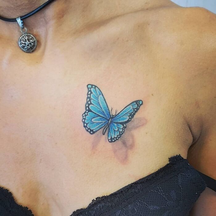 Colorful butterfly tattoo on a person's chest, showcasing vibrant blue wings.