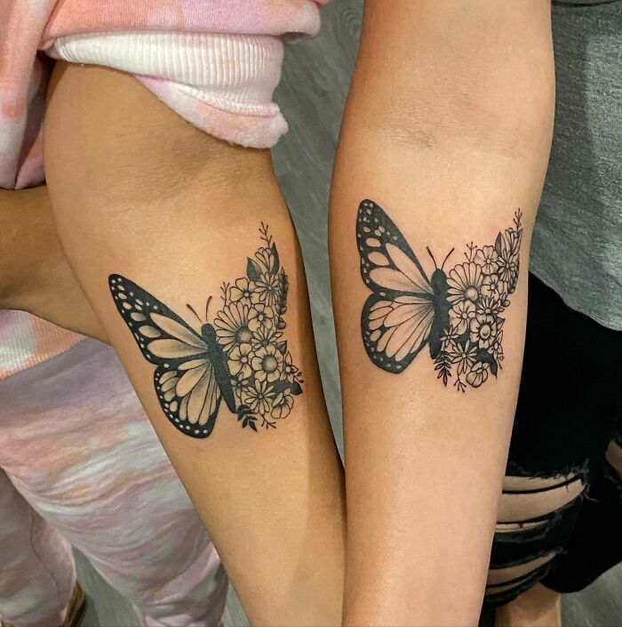 Butterfly tattoos with floral patterns on two forearms.