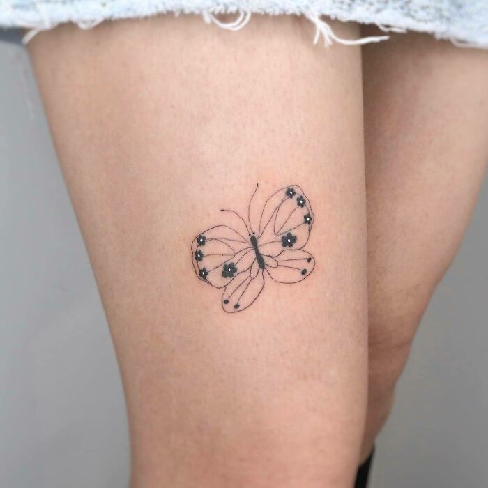 Minimalist butterfly tattoo on thigh, showcasing delicate black ink details.