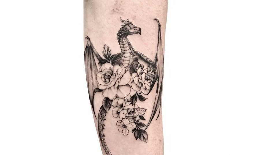 Dragon tattoo with wings and flowers, black and gray design on forearm.