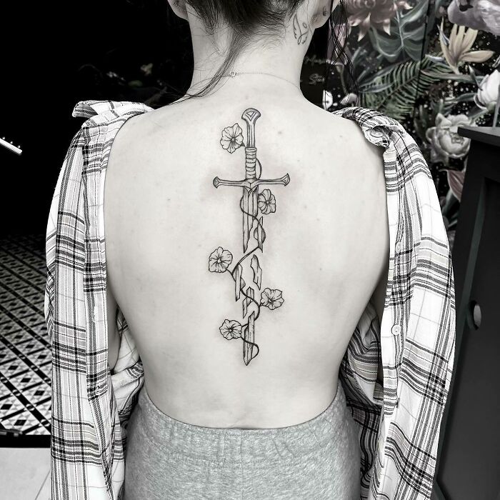 Back tattoo featuring a sword and flowers, inspired by Lord of the Rings design elements.