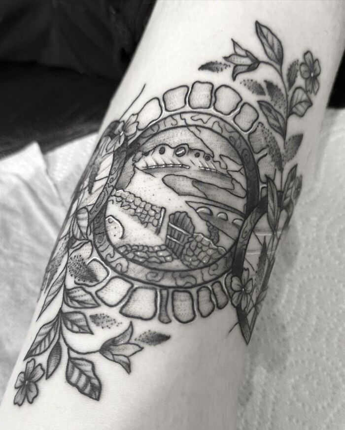Black and grey tattoo of a Hobbit hole from Lord of the Rings, surrounded by leaves and flowers.