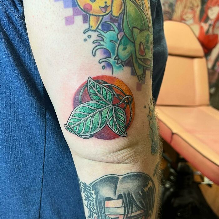 Lord of the Rings tattoo of leaves on an arm, colorful and detailed, surrounded by other tattoos, in a tattoo studio.