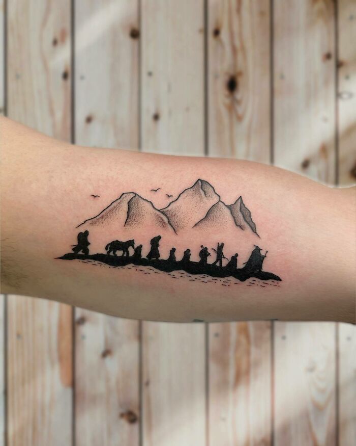 "Minimalist Lord of the Rings tattoo featuring the Fellowship silhouette against mountain backdrop on forearm."